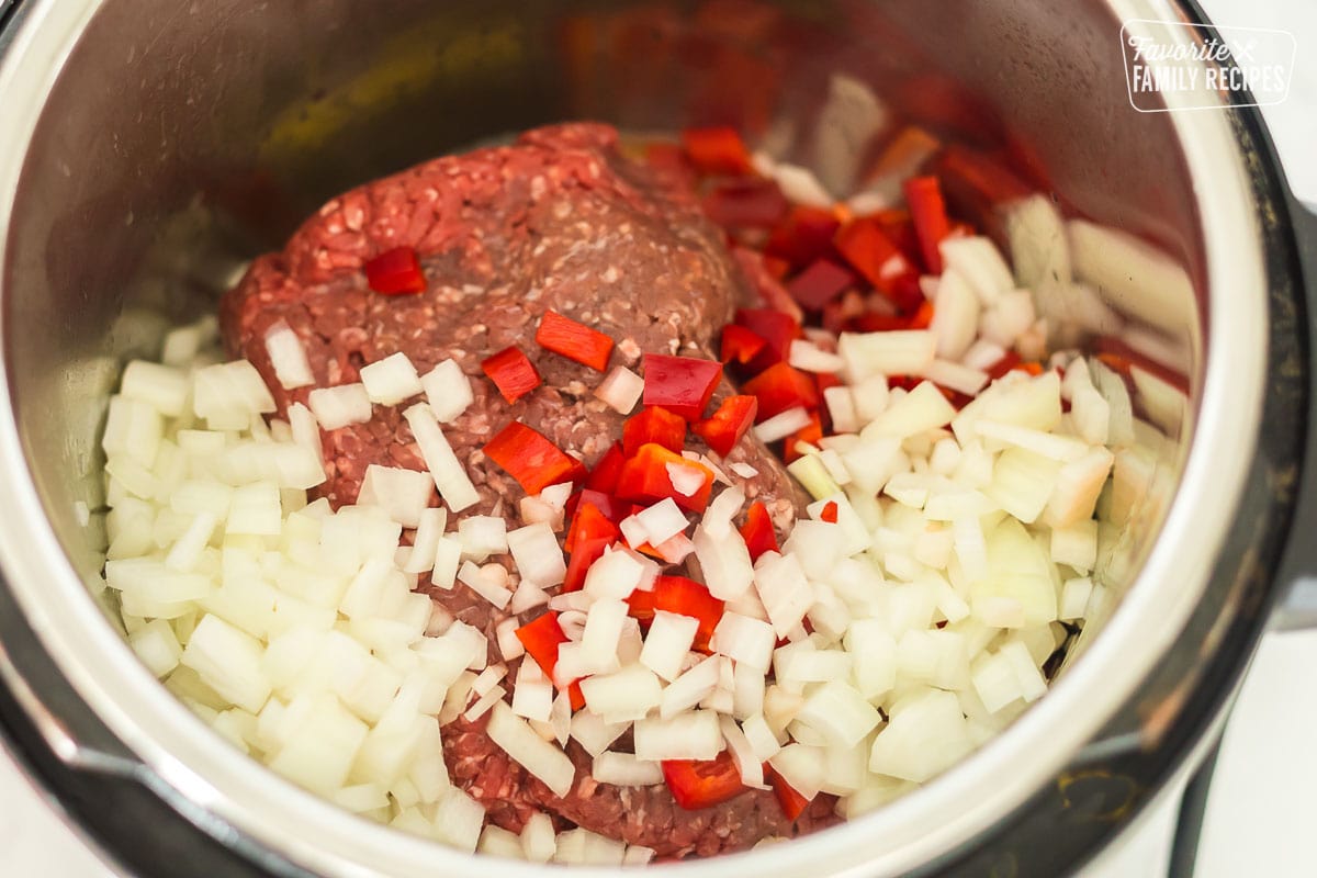 Ground beef in an Instant Pot with chopped onion and red bell peppers