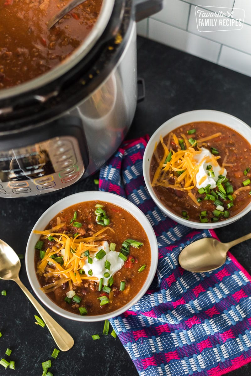 Tired of spending all day cooking chili? This hearty Instant Pot chili can be made in under an hour. Plus, learn how to avoid the dreaded burn notice! Two bowls of Instant Pot chili next to an Instant pot.