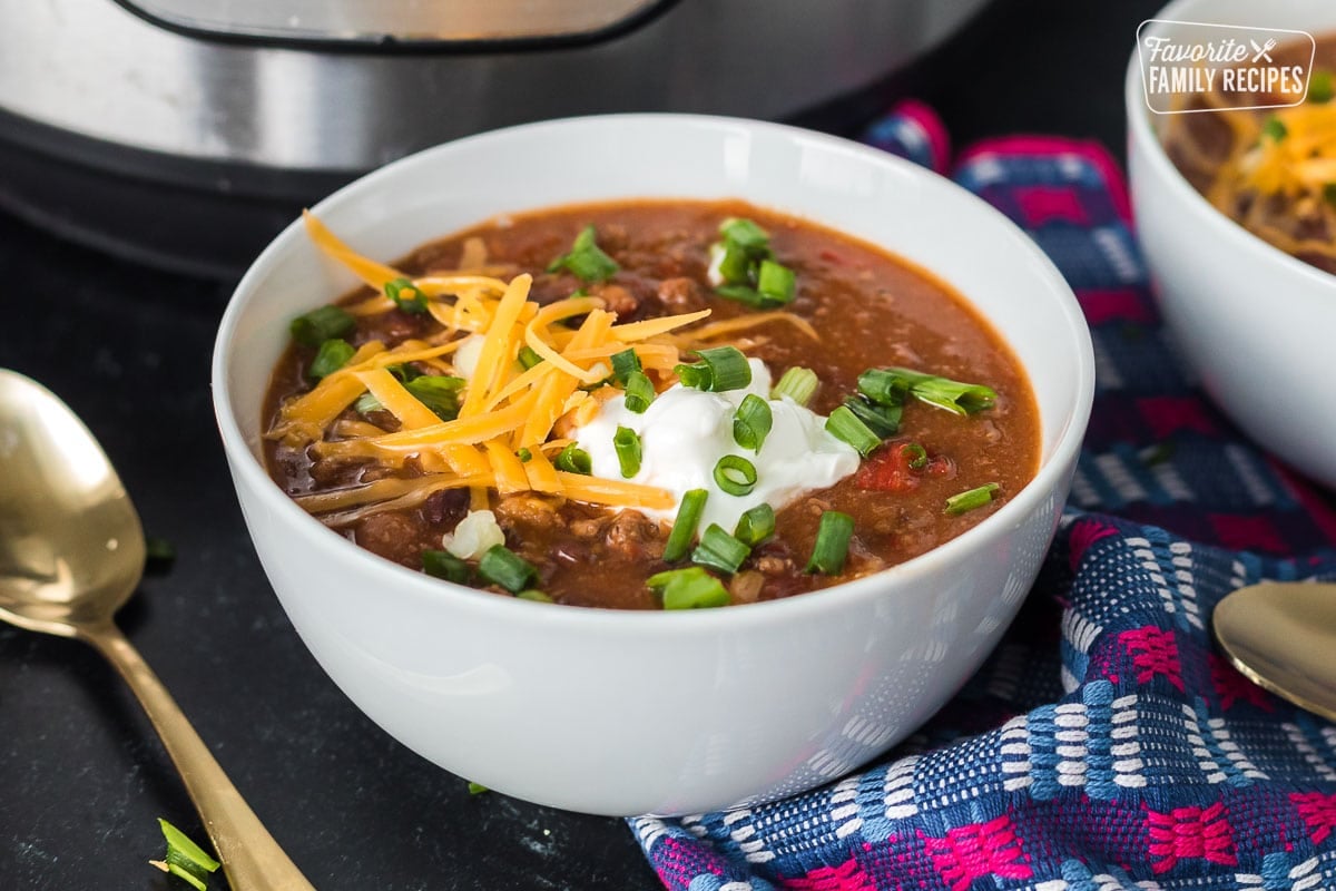 A close up of a bowl of chili with sour cream and shredded cheese over the top.