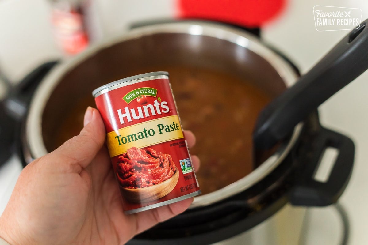 A hand holding a can of tomato paste.