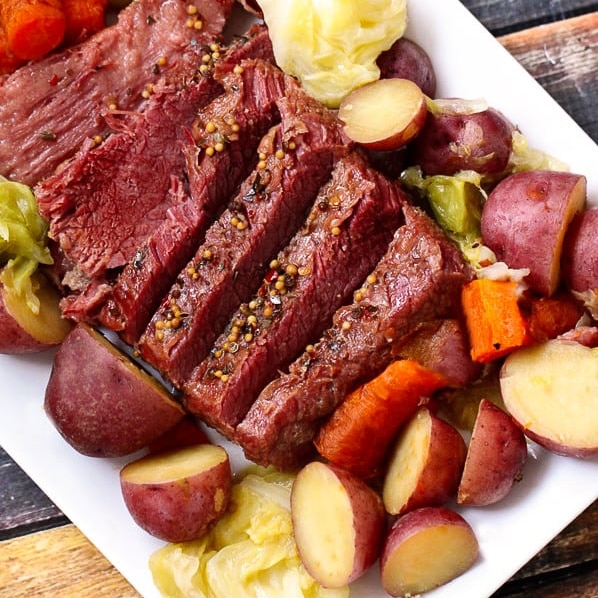 Corned beef on a white platter with vegetables on the side
