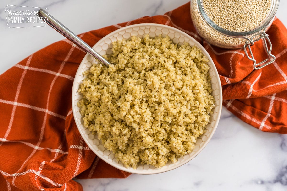 A bowl of quinoa with a jar of uncooked quinoa next to it.