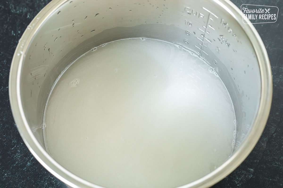 An Instant Pot liner with rice in the process of being rinsed
