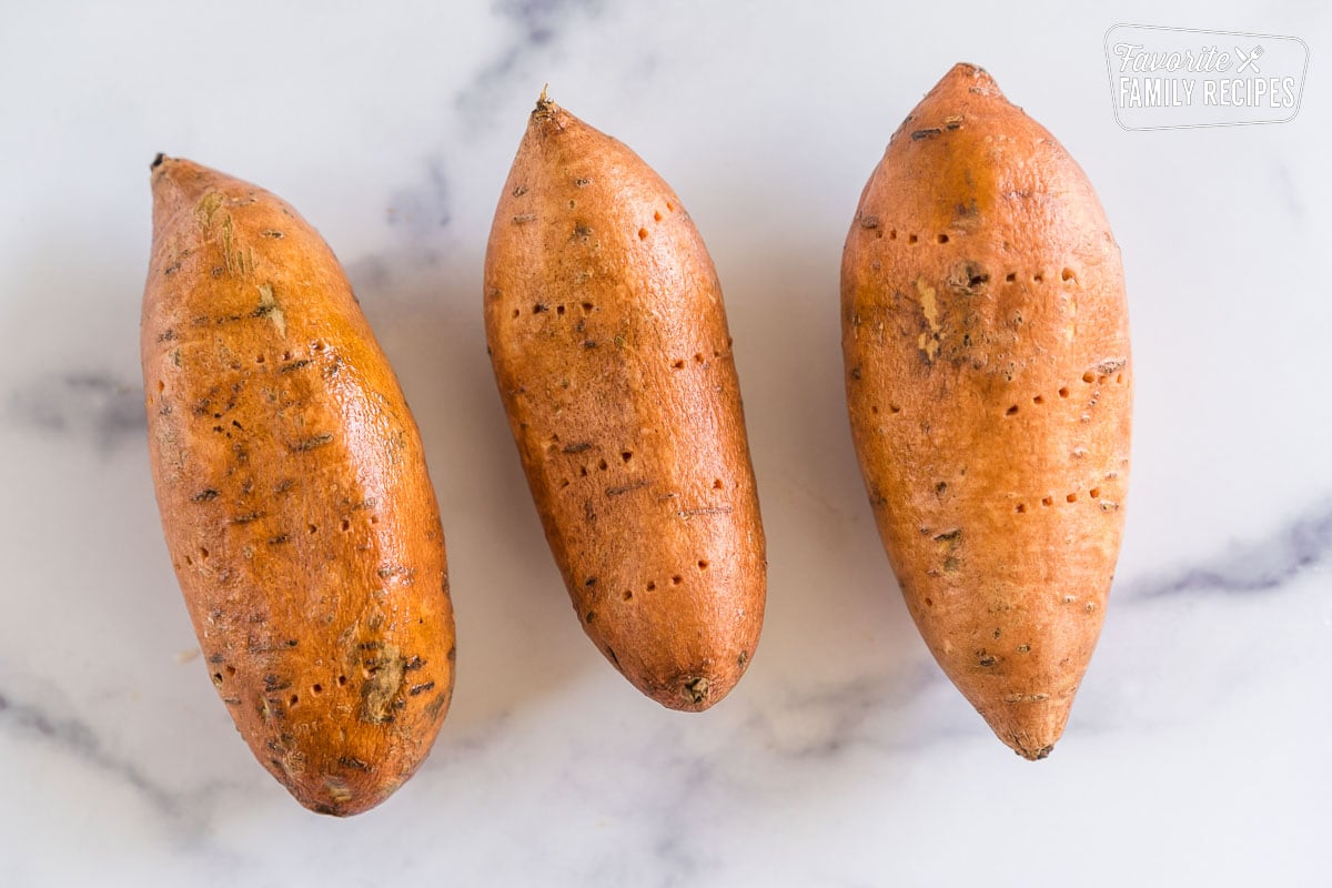 Three raw sweet potatoes with holes poked in them with a fork.