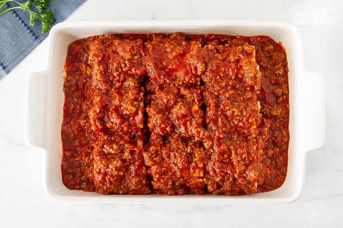 Lasagne Roll Ups in a dish covered with Italian sausage sauce.