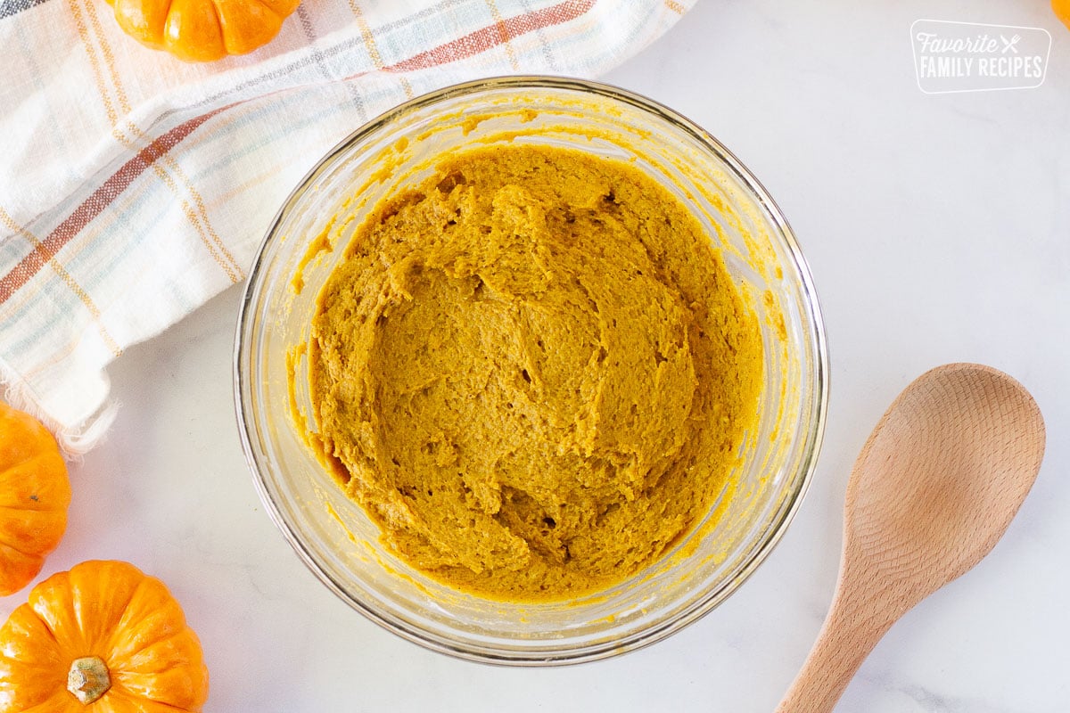 Bowl of cake mix and pumpkin mixed together to make Pumpkin Chocolate Chip Cookies. Wooden spoon on the side and mini pumpkins.