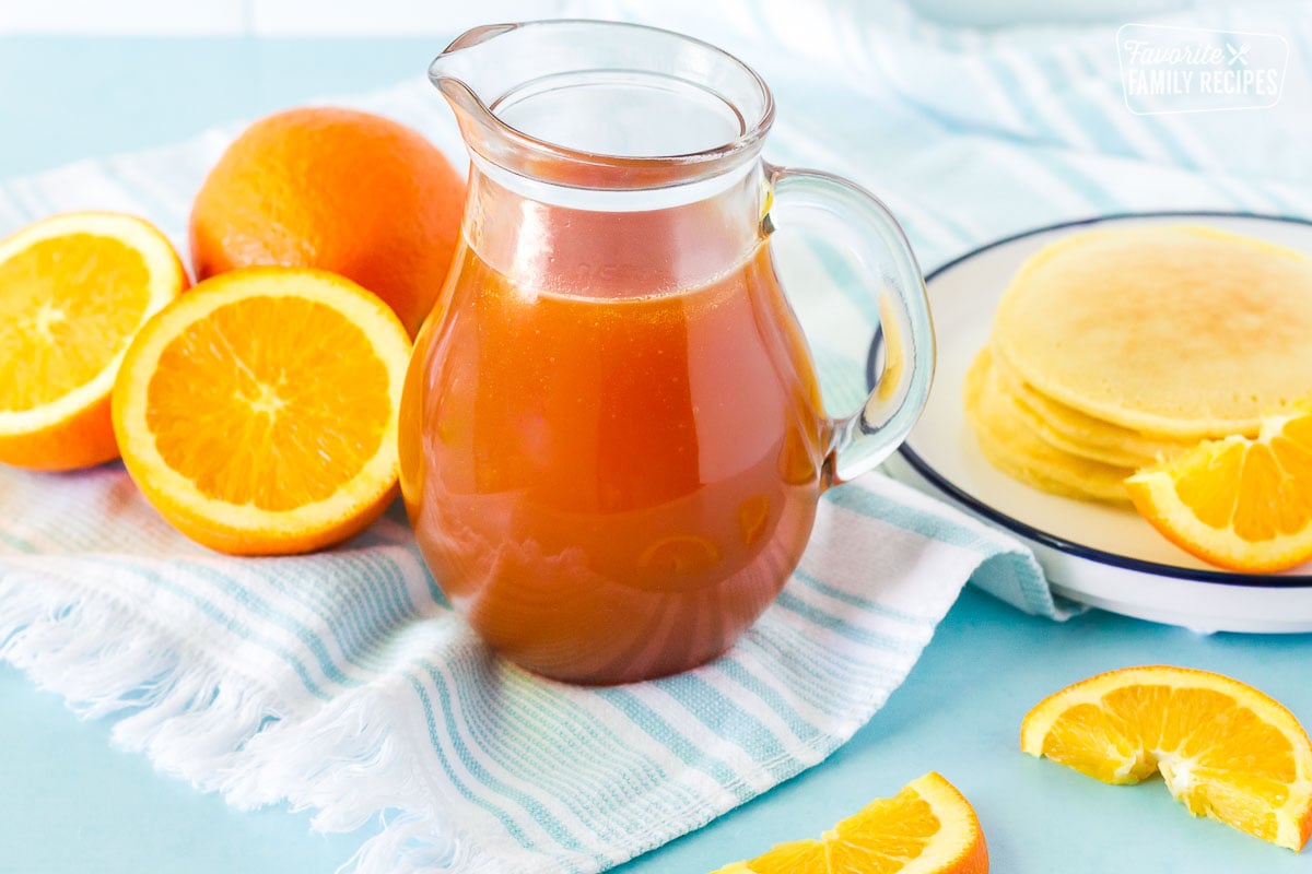 Orange Syrup in a pitcher with pancakes and fresh oranges.
