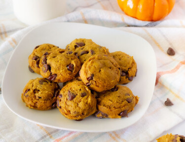 Pumpkin Chocolate Chip Cookies on a plate with a glass of milk and extra cookies on the side.