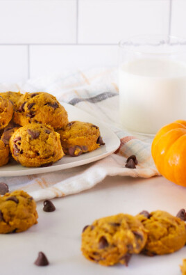 Fresh Pumpkin Chocolate Chip Cookies on a plate with a side of milk. Mini pumpkins and extra cookie decorate the table.