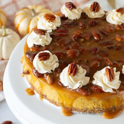 Pumpkin Cheesecake on a cake platter with caramel pecan and whipped cream.
