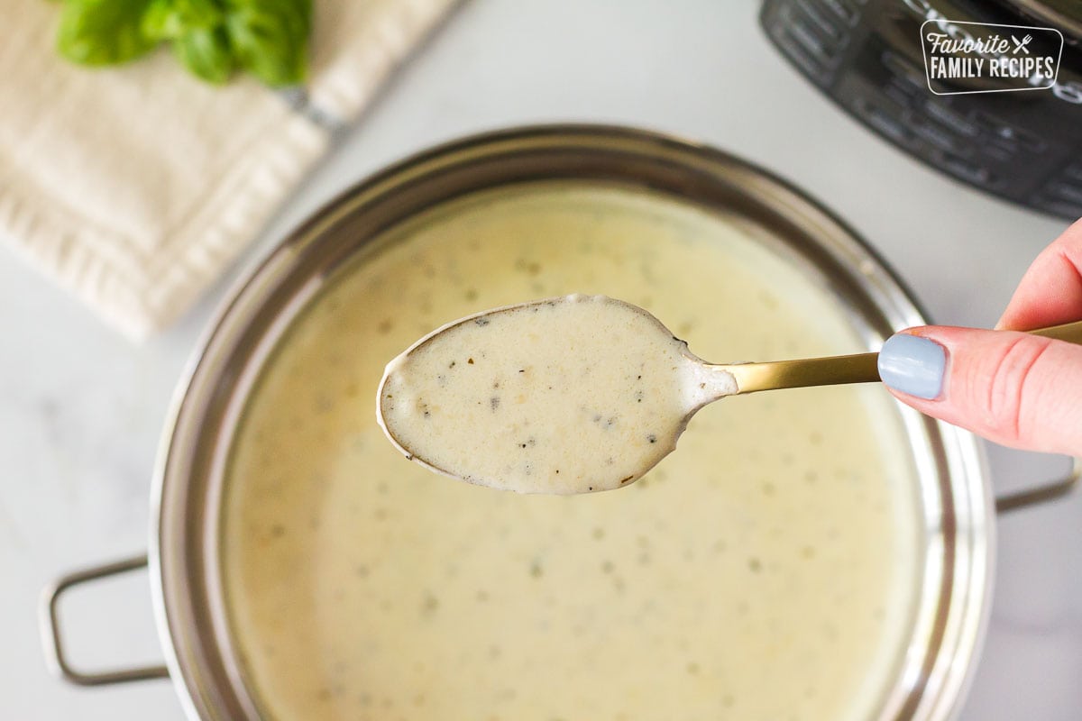 Spoon holding creamy basil sauce for Instant Pot Chicken and Rice.