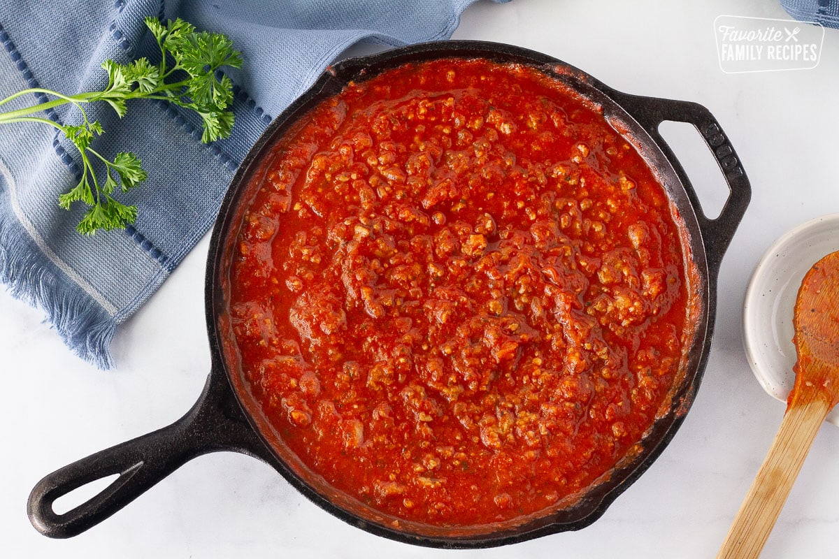 Skillet with sauce to make Lasagne Roll Ups. Wooden spoon on the side.