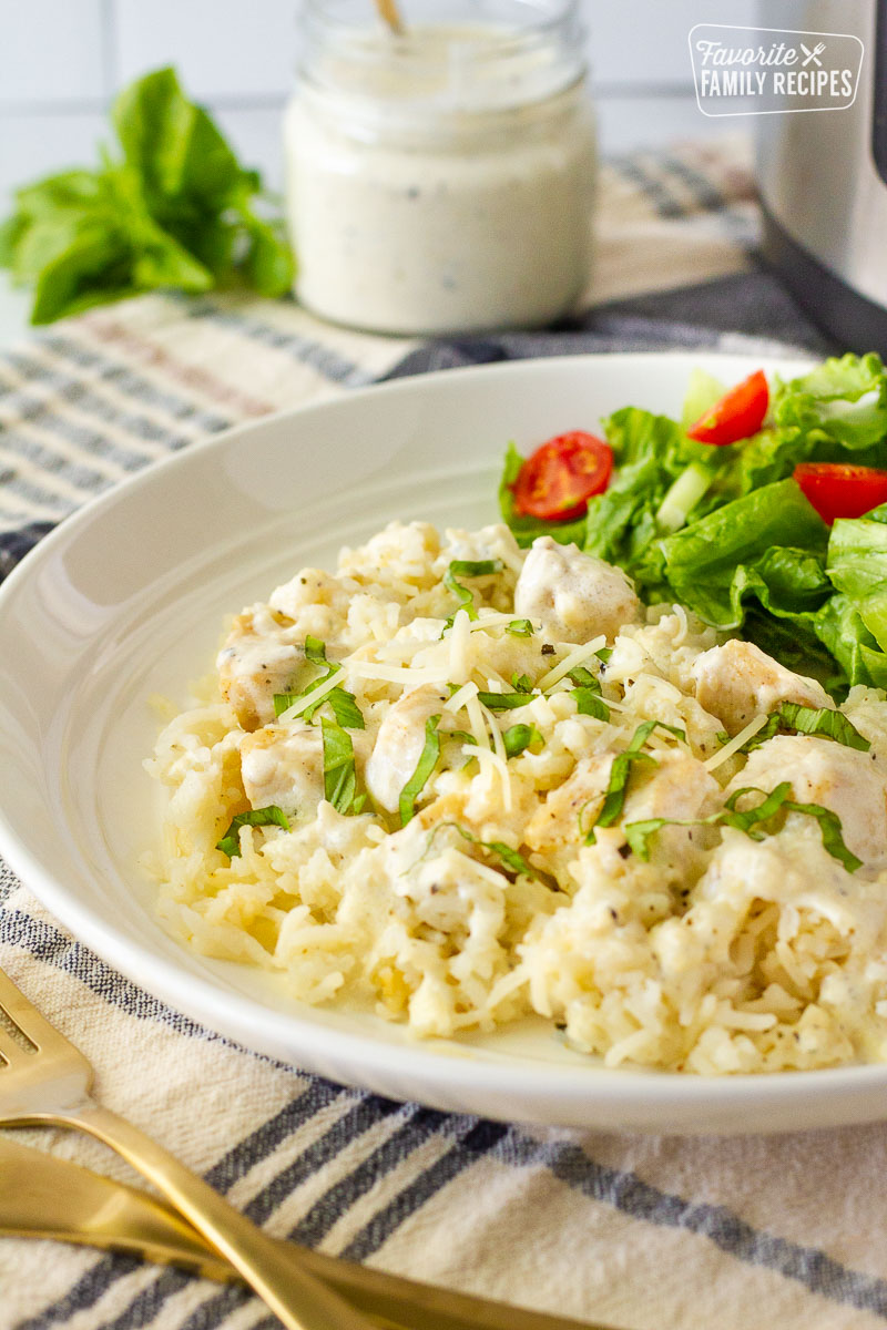 Side view of Instant Pot Chicken and Rice on a plate with a side salad. Instant pot and creamy sauce on the side.