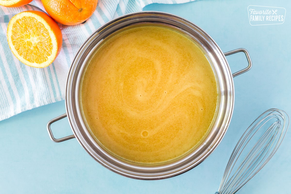 Thickened Orange Syrup in a pan with a whisk on the side.