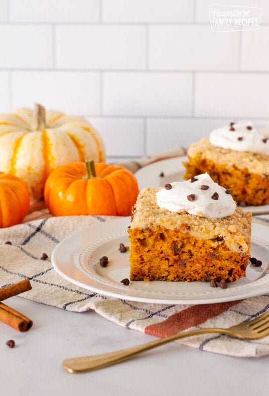 Two slices of Pumpkin Coffee Cake on plates. Both topped with whipped cream and mini chocolate chips.