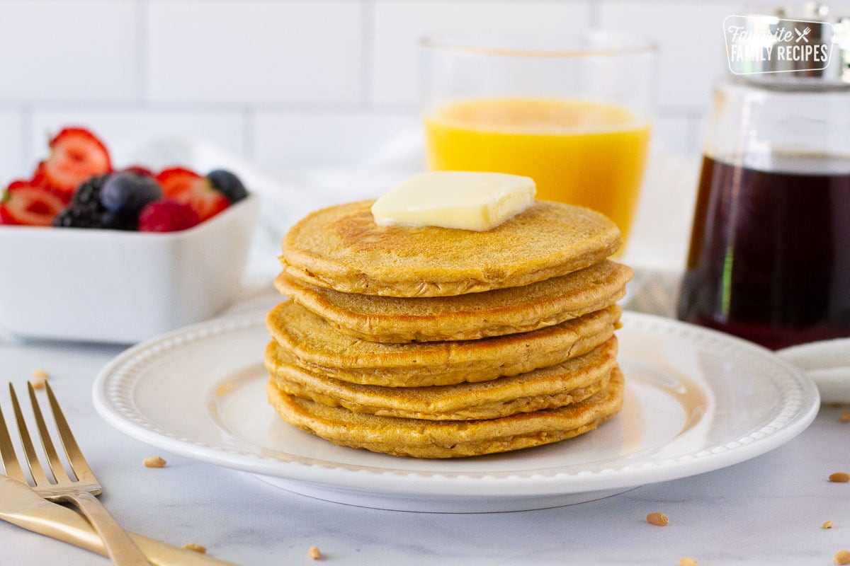 Whole Wheat Pancakes in a stack with fruit, juice and syrup on the side.