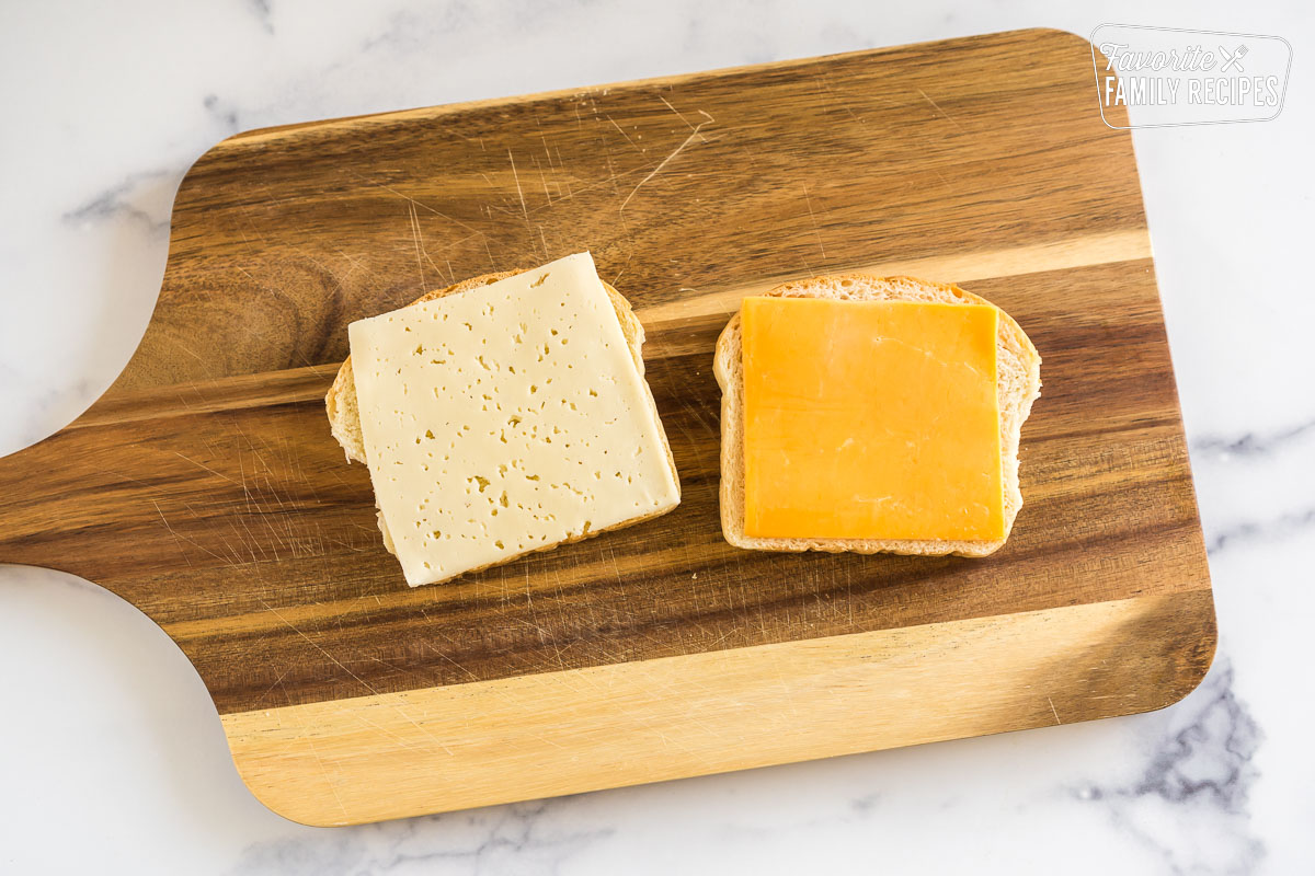 two slices of bread on a cutting board with a slice of cheese on each slice of bread