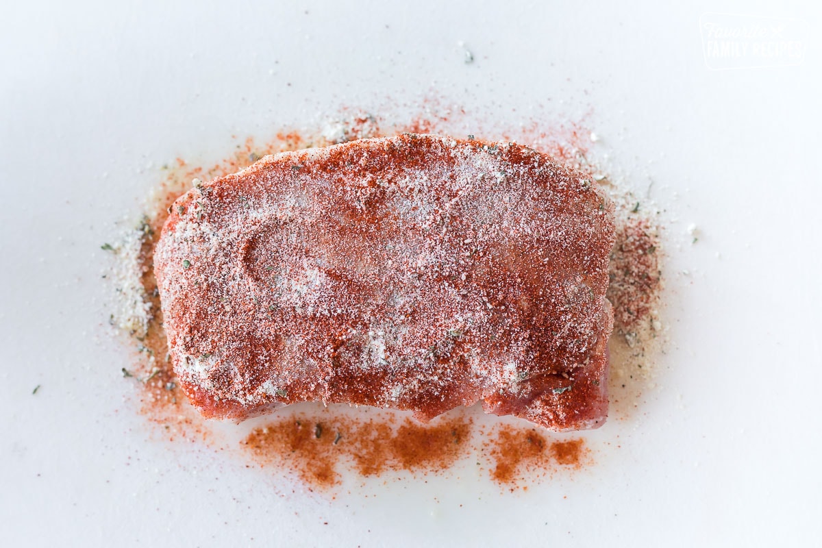 A raw pork chop seasoned with salt, ranch seasoning, and paprika