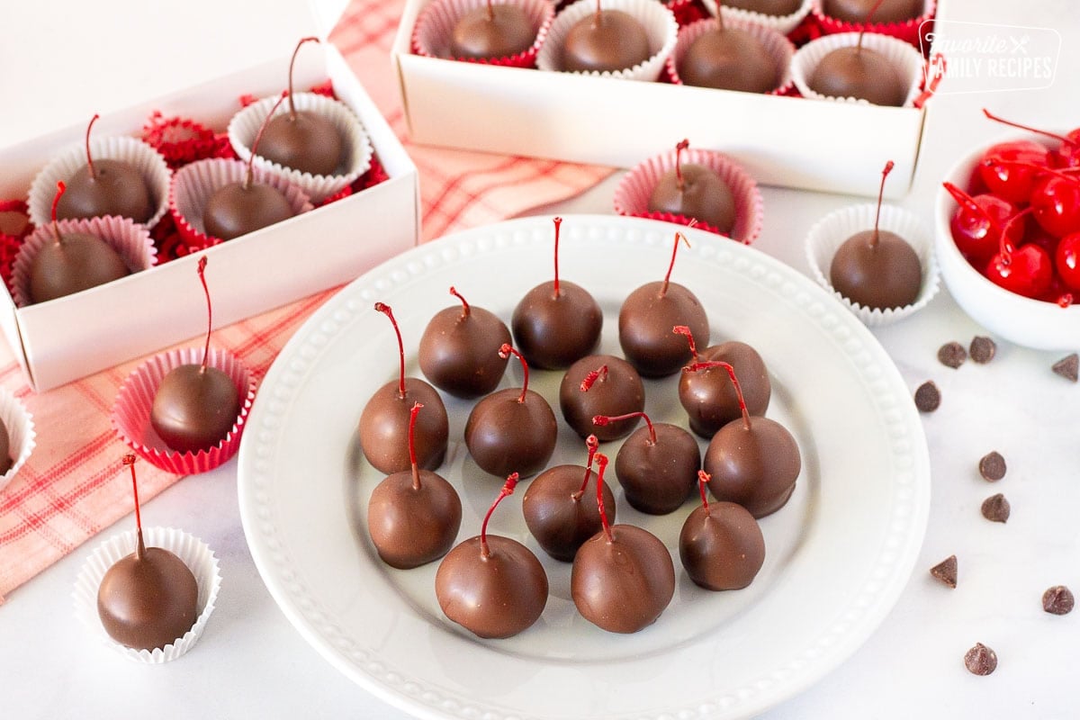 Plate of Chocolate Covered Cherries next to gift boxes of chocolate covered cherries.