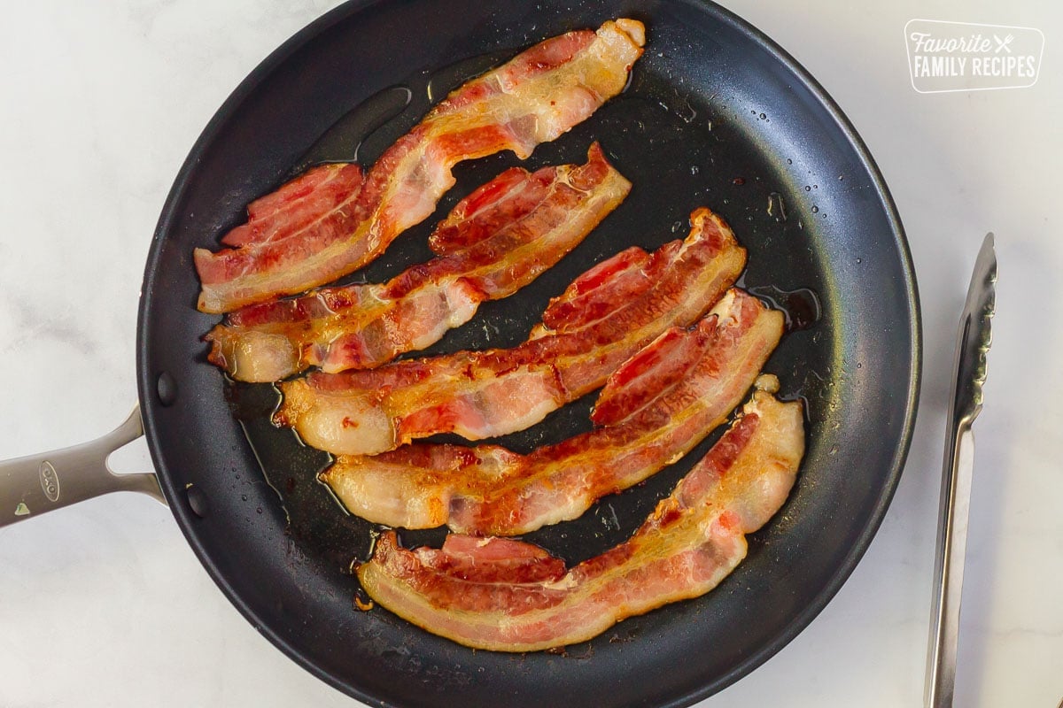 Pan of bacon cooking with tongs on the side for Green Bean Casserole.