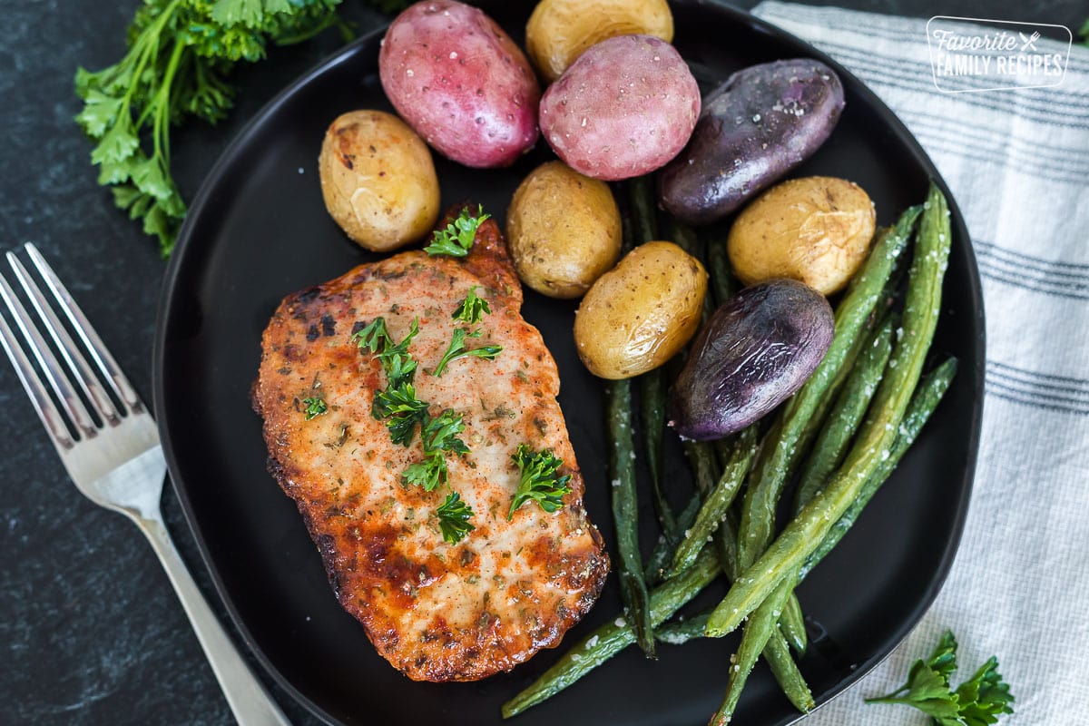 A pork chop on a plate with roasted gem potatoes and green beans.