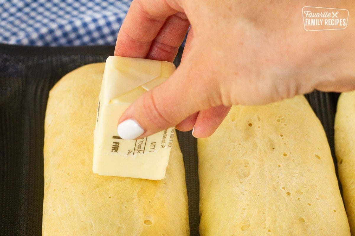 Hand rubbing cube of butter on top of hot Subway Bread.