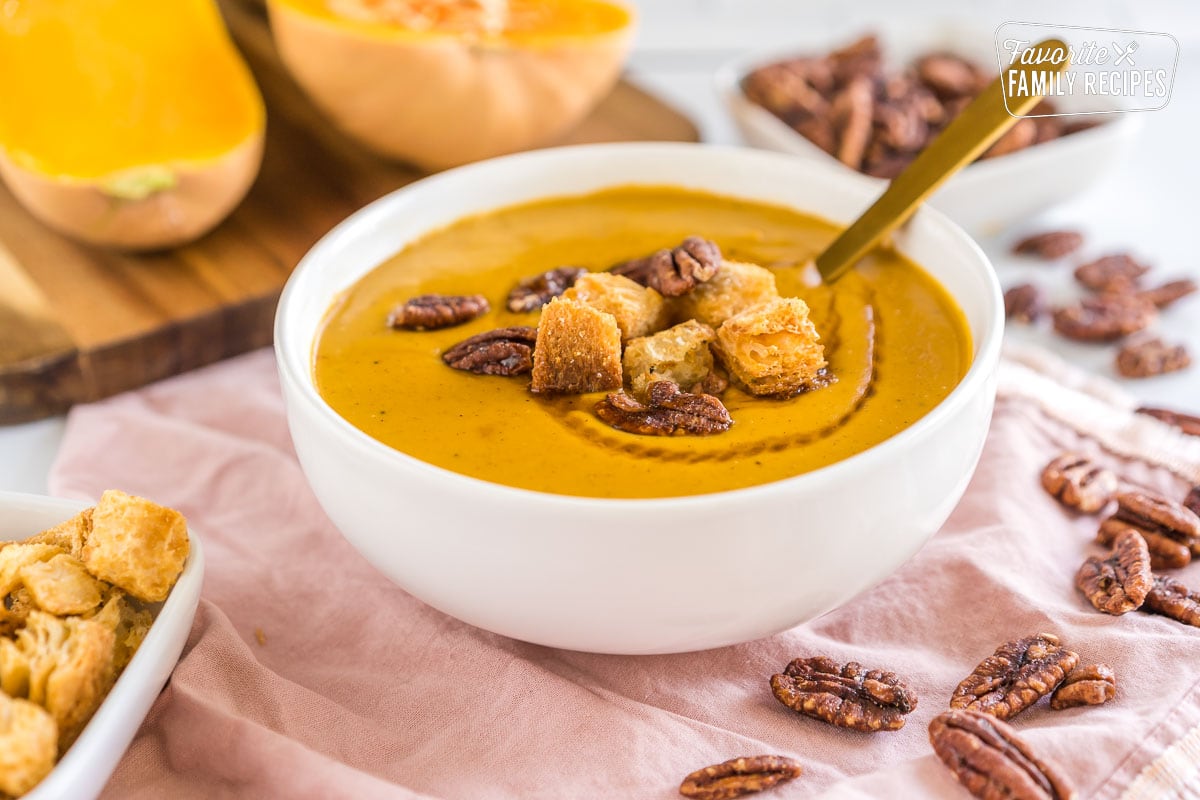 A bowl of butternut squash soup topped with croutons and nuts.