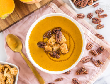 Butternut squash soup in a white bowl garnished with croutons and pecans.