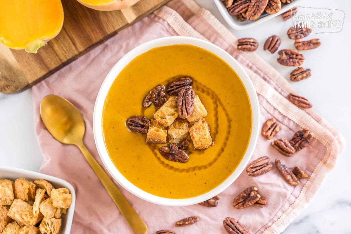 Butternut squash soup in a white bowl garnished with croutons and pecans.