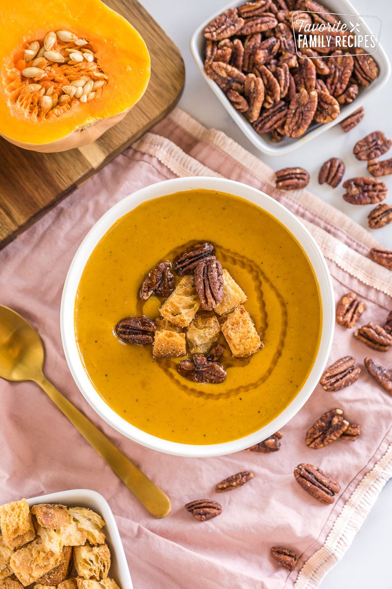 A bowl of butternut squash soup topped with croutons and nuts.