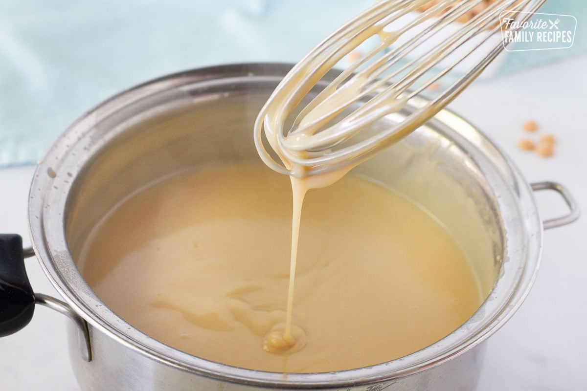 Whisk showing drizzle of hot Butterscotch Pie filling in a pan.