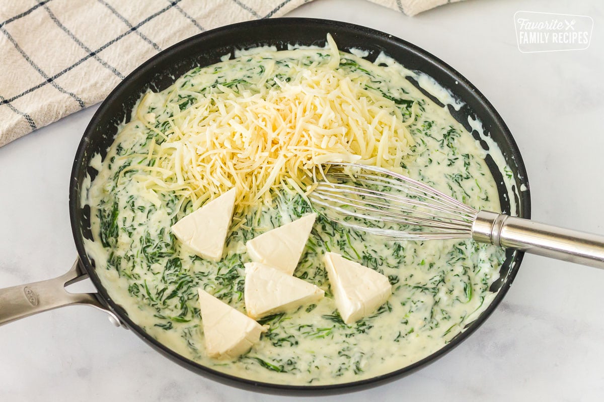 Pan of spinach and sauce with unmelted cheeses on top to make Creamed Spinach.