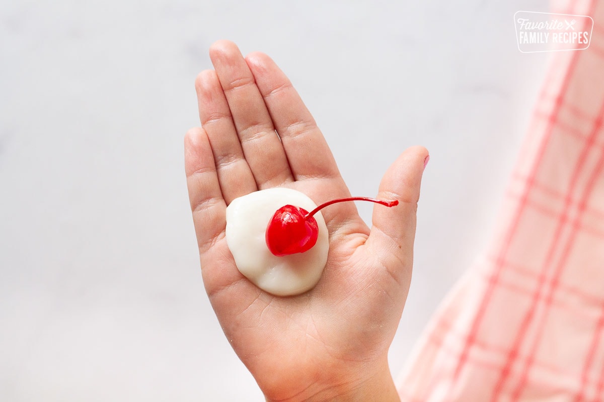 Hand holding a cherry on top of the fondant circle for Chocolate Covered Cherries.