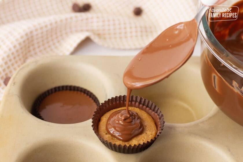 Spoon pouring melted chocolate on top of the Homemade Reese's Peanut Butter Cup.