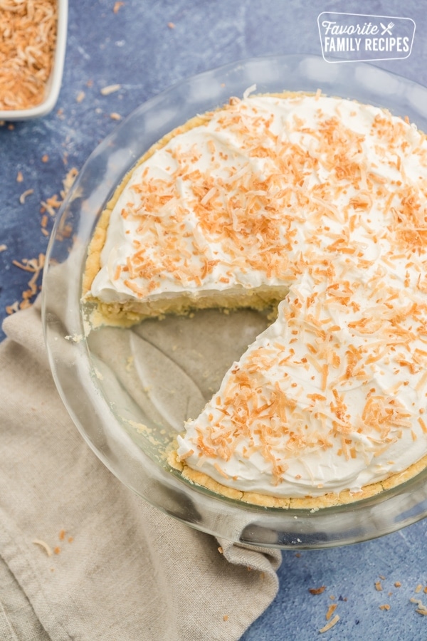 A coconut cream pie with a slice out of it with toasted coconut on top.