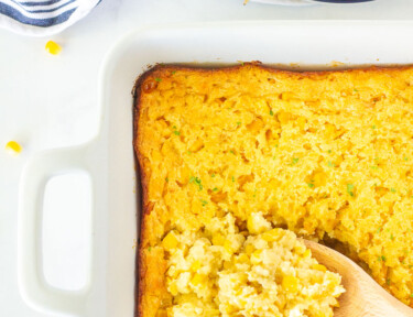 Wooden spoon scooping Corn Casserole from the baking dish.