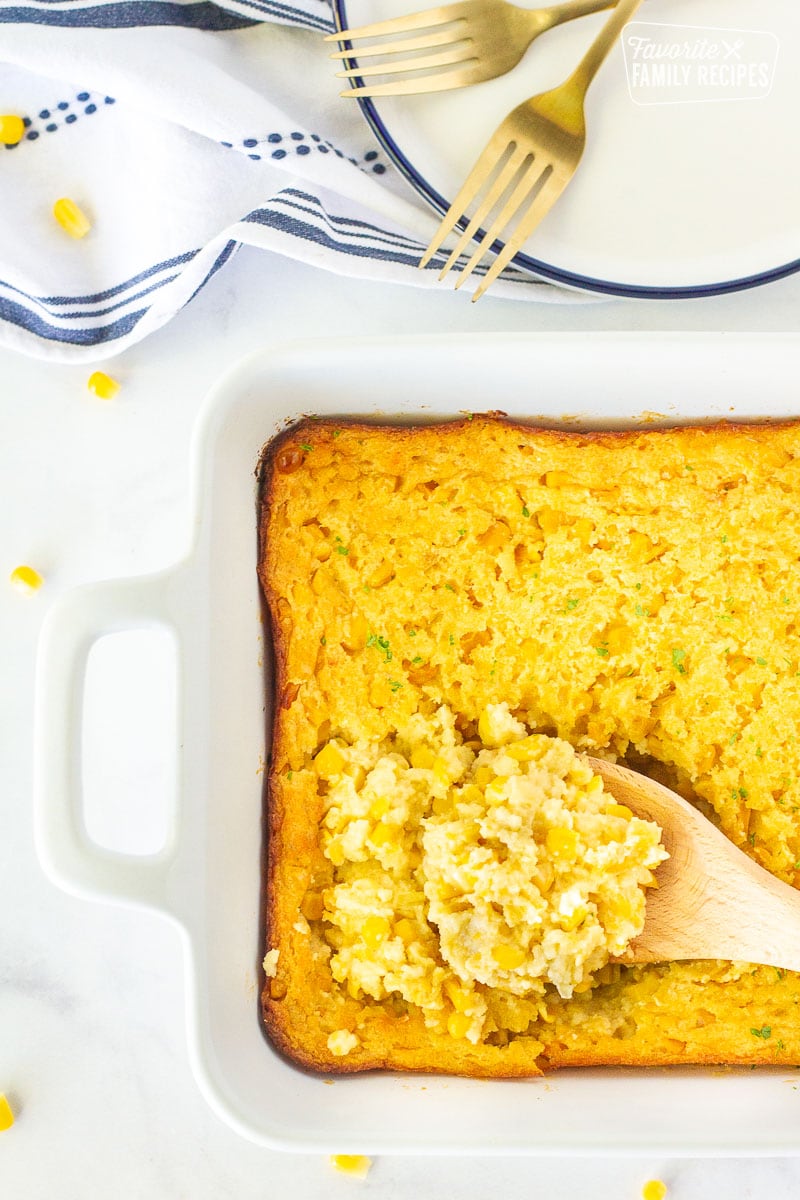 Wooden spoon scooping Corn Casserole from the baking dish.