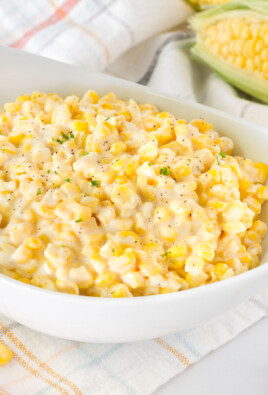 Bowl of Creamed Corn with a wooden spoon and fresh corn on the side.