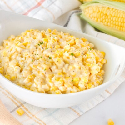 Bowl of Creamed Corn with a wooden spoon and fresh corn on the side.