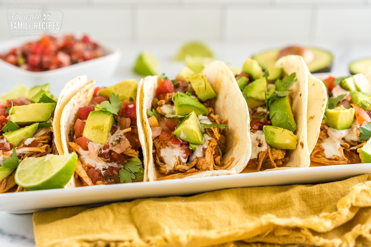 A tray of crockpot chicken tacos topped with avocado, crema, and cilantro