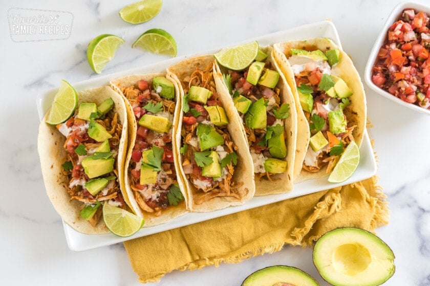 A tray of crockpot chicken tacos topped with avocado, crema, and cilantro