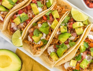 A tray of crockpot chicken tacos topped with avocado, crema, and cilantro