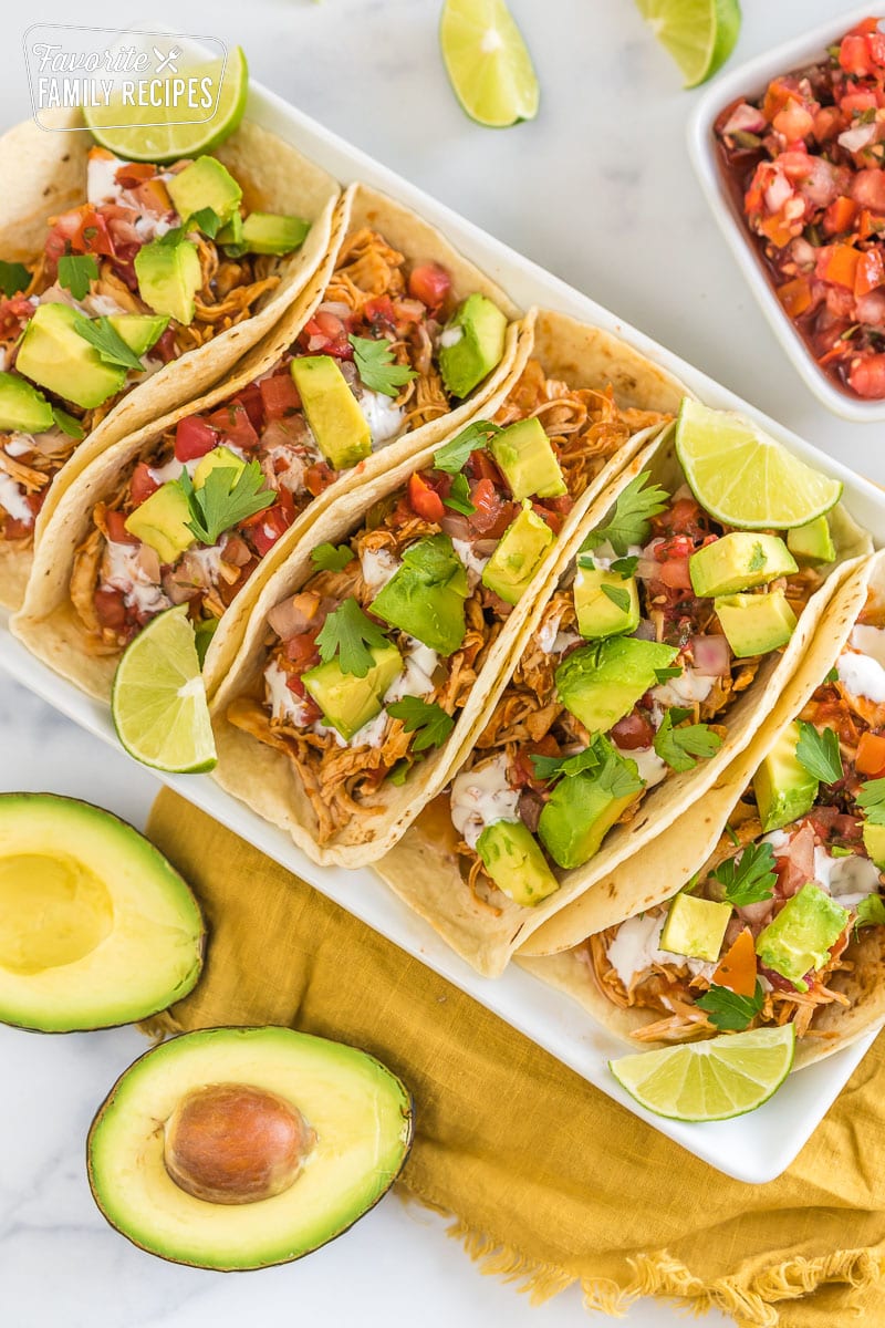 A tray of crockpot chicken tacos topped with avocado, crema, and cilantro