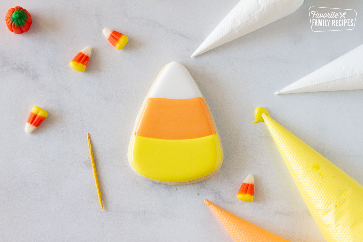 Decorated Candy Corn Halloween cookie next to a toothpick and piping bags.