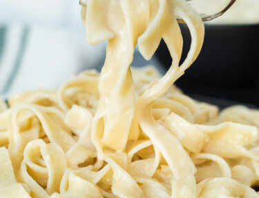 A fork lifting fettuccine Alfredo noodles from a plate showing the smooth creamy texture