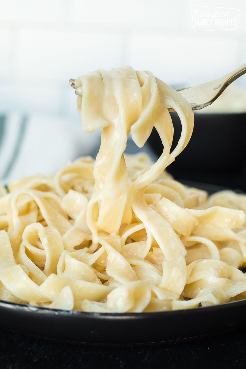 A fork lifting fettuccine Alfredo noodles from a plate showing the smooth creamy texture
