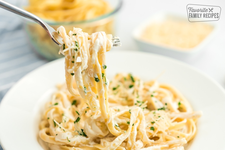 Fettuccine Alfredo wrapped around a fork and being pulled up from a plate of pasta.