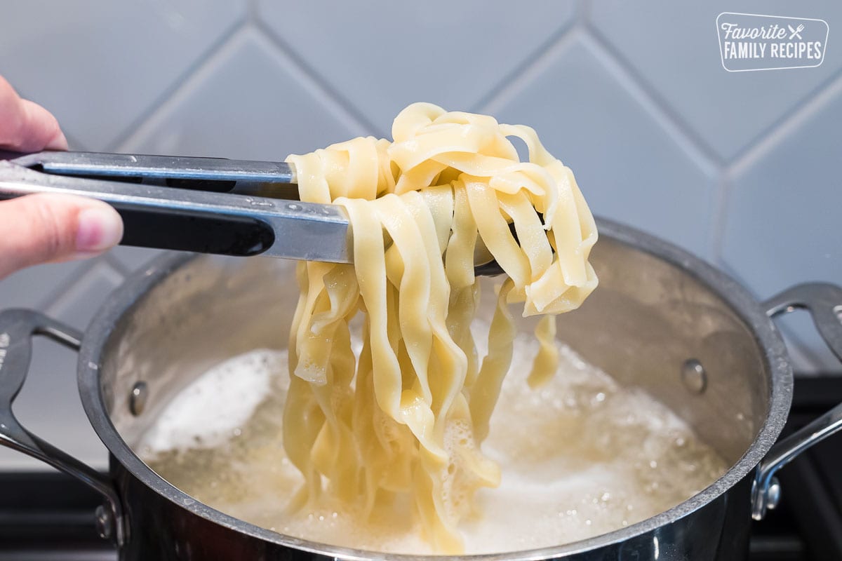 Fettuccine noodles being lifted from a pot of boiling water