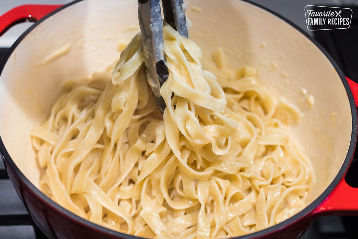 Fettuccine Alfredo being lifted from a pot with tongs
