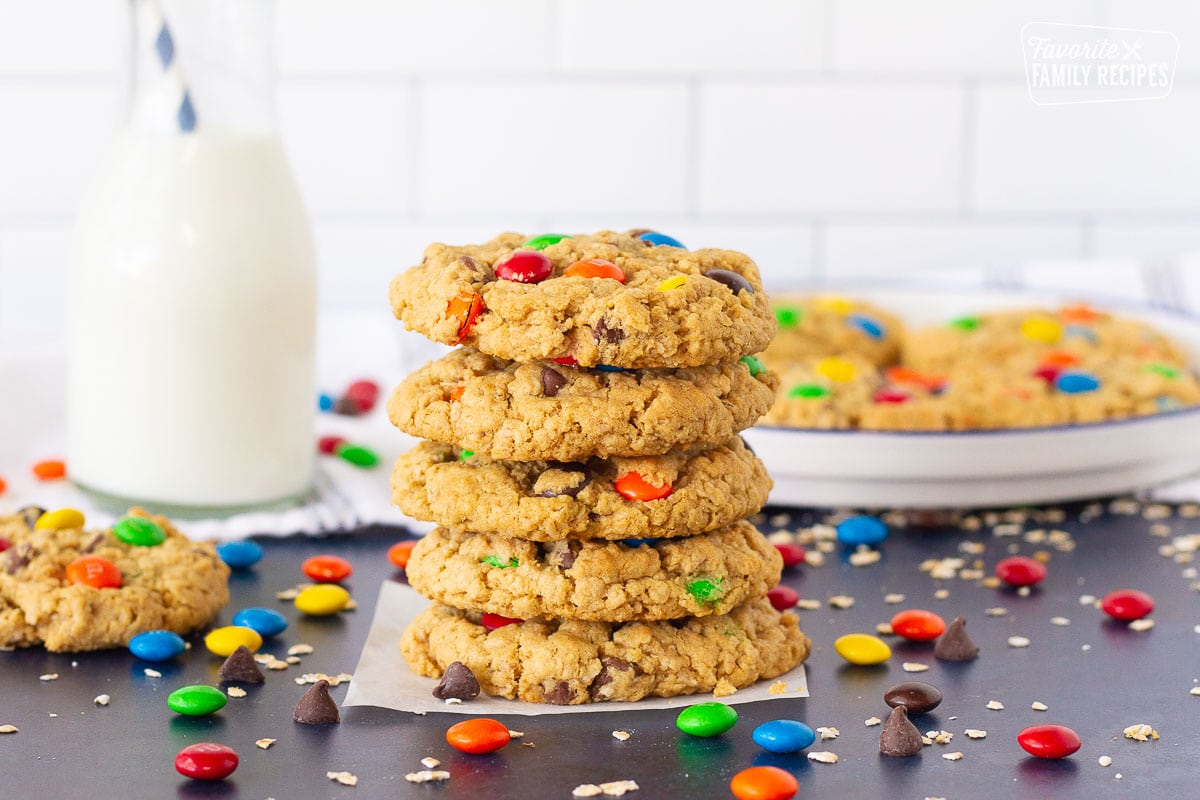 Stack of five Monster Cookies with a plate of cookies and glass of milk in the background.